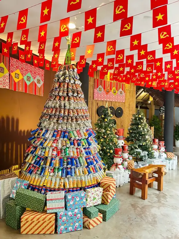 Cây thông Noel xếp từ vỏ lon tái chế bên hộp quà và cây thông nhỏ – Giáng sinh 2025 ở Serena Kim Bôi