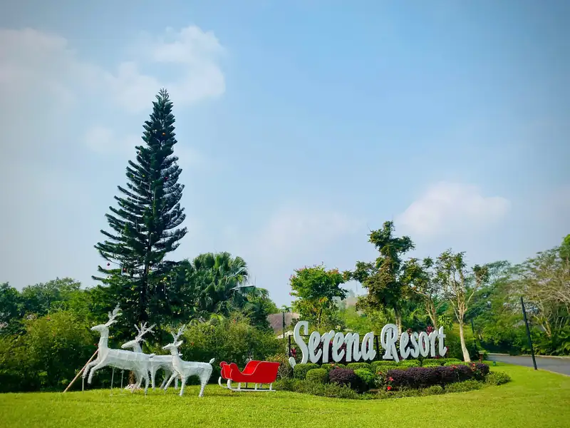Tuần lộc trắng, xe trượt tuyết đỏ cạnh cây thông và biển tên Serena Resort trên bãi cỏ dịp Giáng sinh 2025