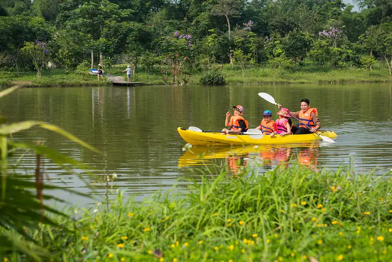 Gia đình mặc áo phao chèo thuyền kayak trên hồ giữa vườn cây ở Serena Kim Bôi
