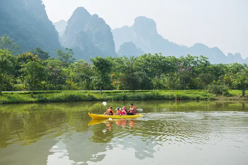 Gia đình mặc áo phao chèo thuyền kayak vàng trên hồ dưới núi đá vôi ở Serena Kim Bôi