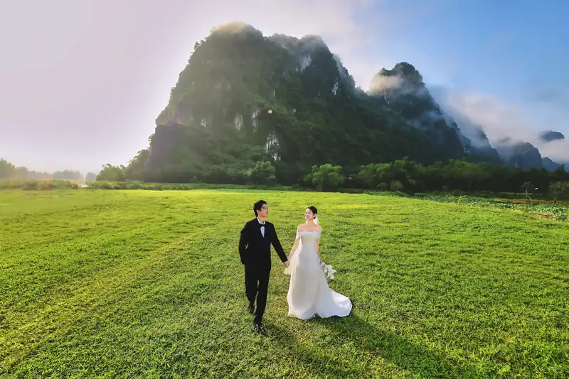 Cô dâu chú rể đi trên bãi cỏ rộng dưới núi đá vôi – chụp ảnh cưới ở Serena Kim Bôi
