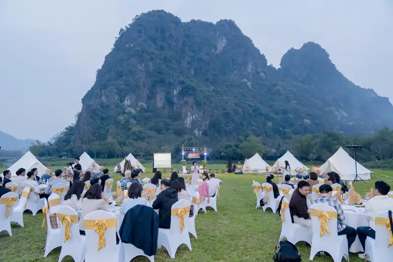 Đoàn khách dự tiệc ngoài trời trên bãi cỏ, lều trắng và núi đá vôi phía sau – Serena Resort Kim Bôi