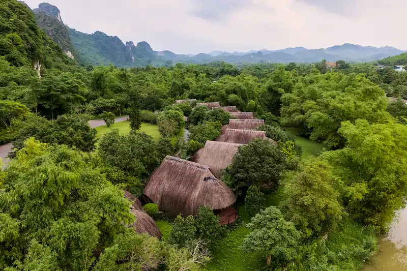 Dãy nhà mái tranh nằm giữa vườn cây rậm, núi đá vôi phía sau – Serena Resort Kim Bôi