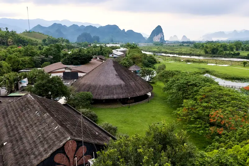 Mái tranh nhà hàng Nón giữa vườn cây, sông Bôi và núi đá vôi phía xa – Serena Kim Bôi