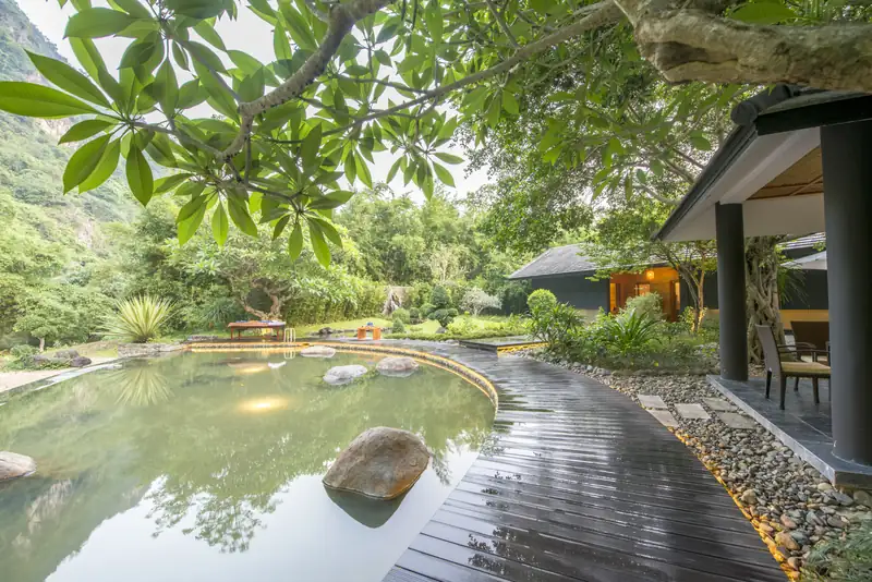 Bể khoáng lát đá bên lối gỗ trong khu onsen kiểu Nhật ở Serena Kim Bôi, núi đá phía sau