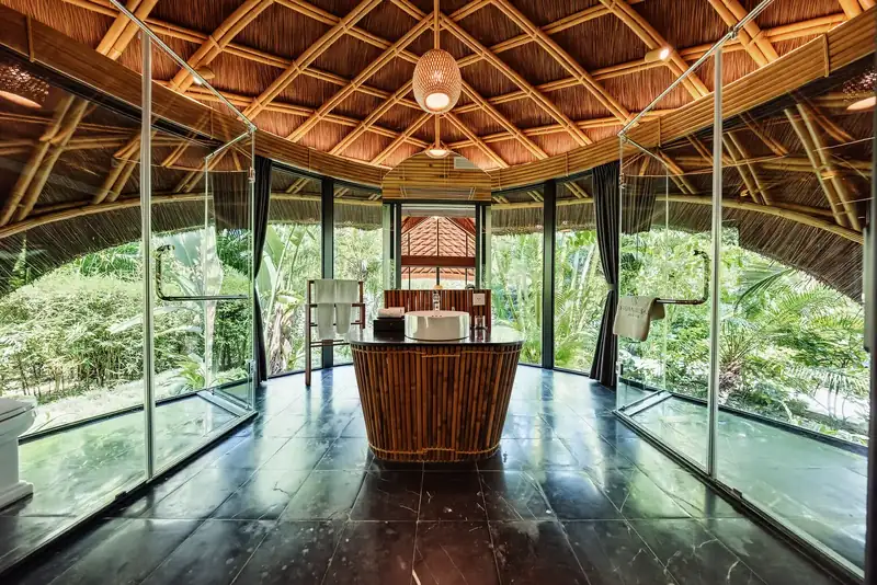 Bàn rửa mặt tròn ốp tre giữa phòng tắm Bungalow, vách kính nhìn ra vườn