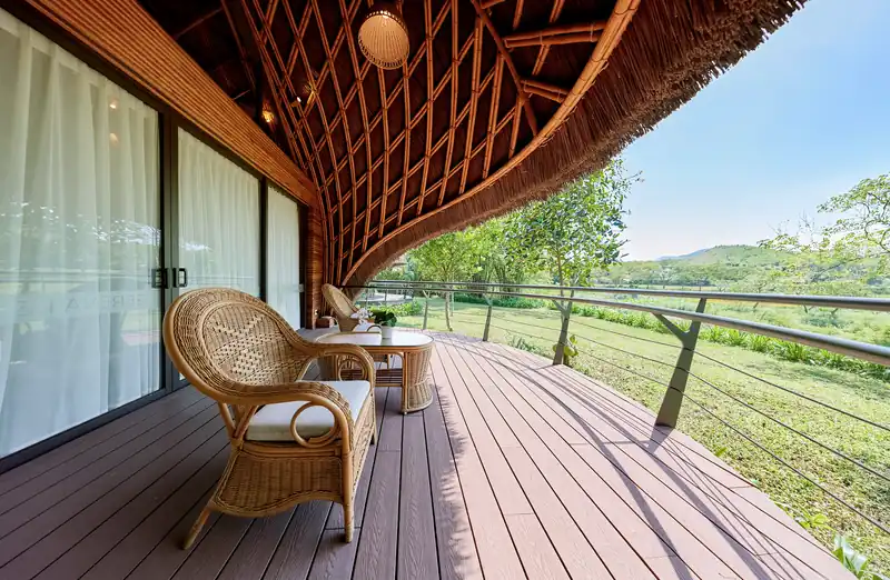 Hiên gỗ Bungalow có ghế mây, mái tre uốn cong, nhìn ra cánh đồng và núi