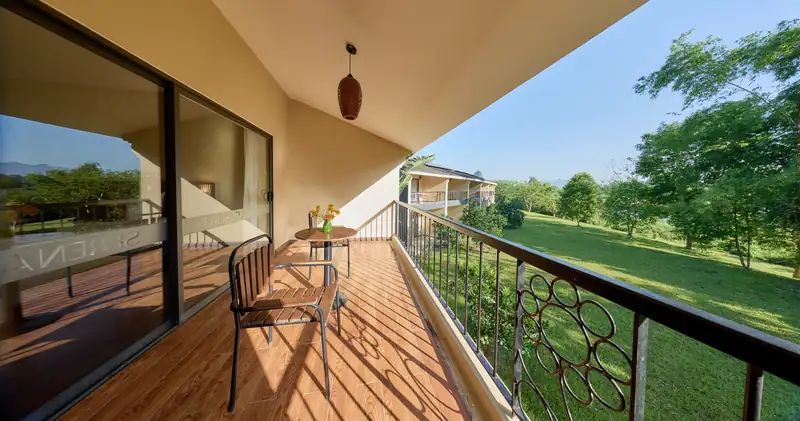 Ban công phòng Deluxe Nature View tầng 2 có bàn ghế, nhìn ra bãi cỏ và hàng cây