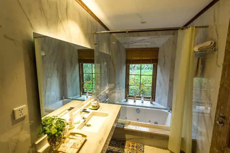 Phòng tắm Osaka Hill ốp đá trắng, bồn Jacuzzi đặt dưới cửa sổ nhìn ra cây xanh