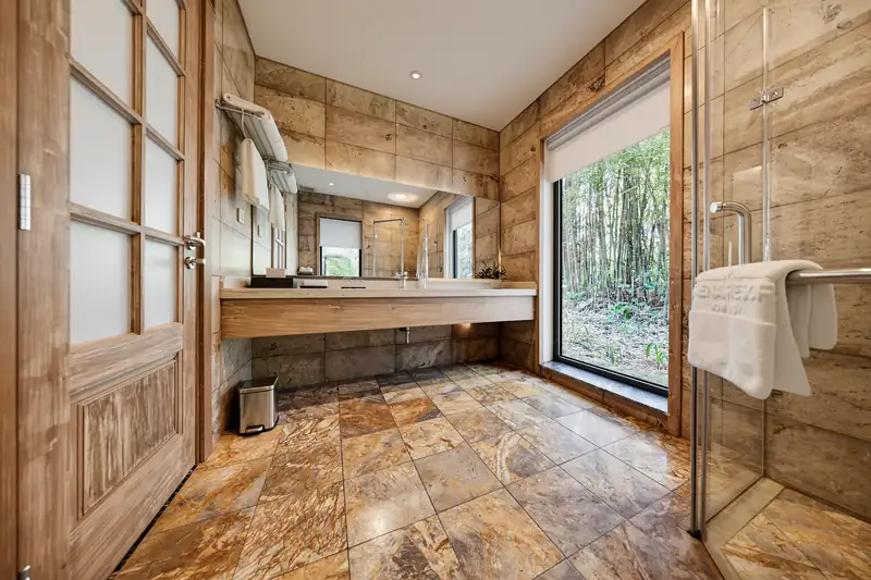Phòng tắm Zen Suite ốp đá, vòi sen vách kính và cửa sổ nhìn rừng tre