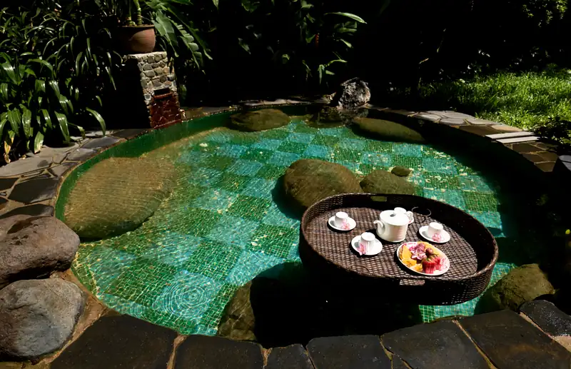 Khay trà và trái cây nổi trên bể onsen đá giữa vườn ở Serena Kim Bôi