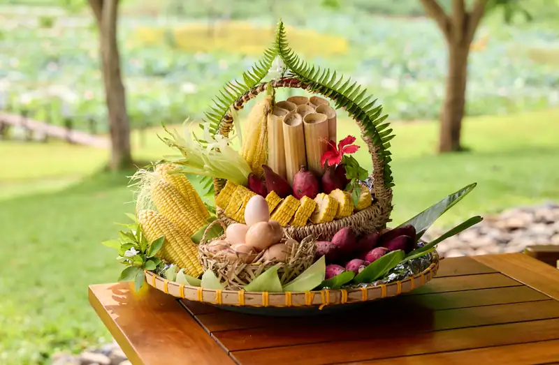 Giỏ đồ nướng ngô, khoai, trứng và cơm lam đặt trên bàn ở khu cắm trại Serena Kim Bôi