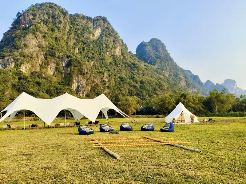 Lều trắng, mái che lớn và hàng ghế lười trên bãi cỏ dưới núi đá vôi ở Serena Kim Bôi