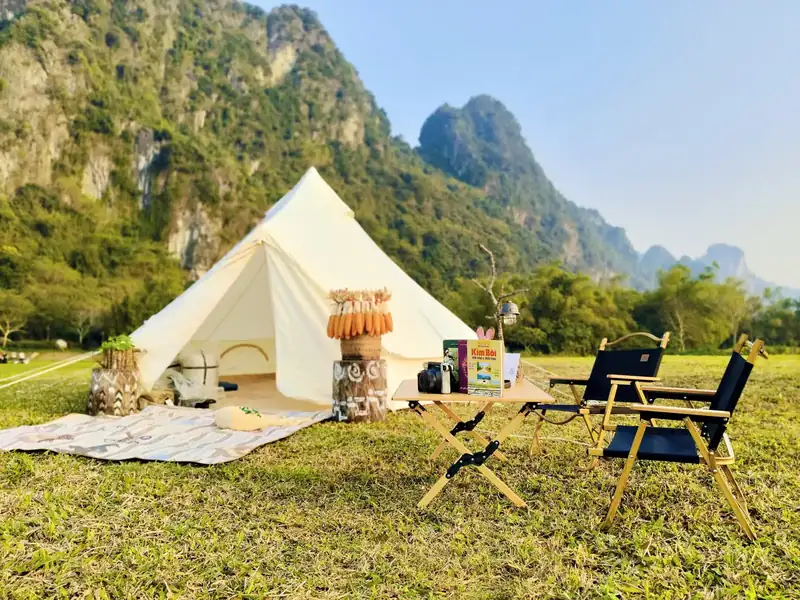 Lều nhỏ, thảm picnic và bộ bàn ghế camping trên bãi cỏ dưới núi đá vôi ở Serena Kim Bôi